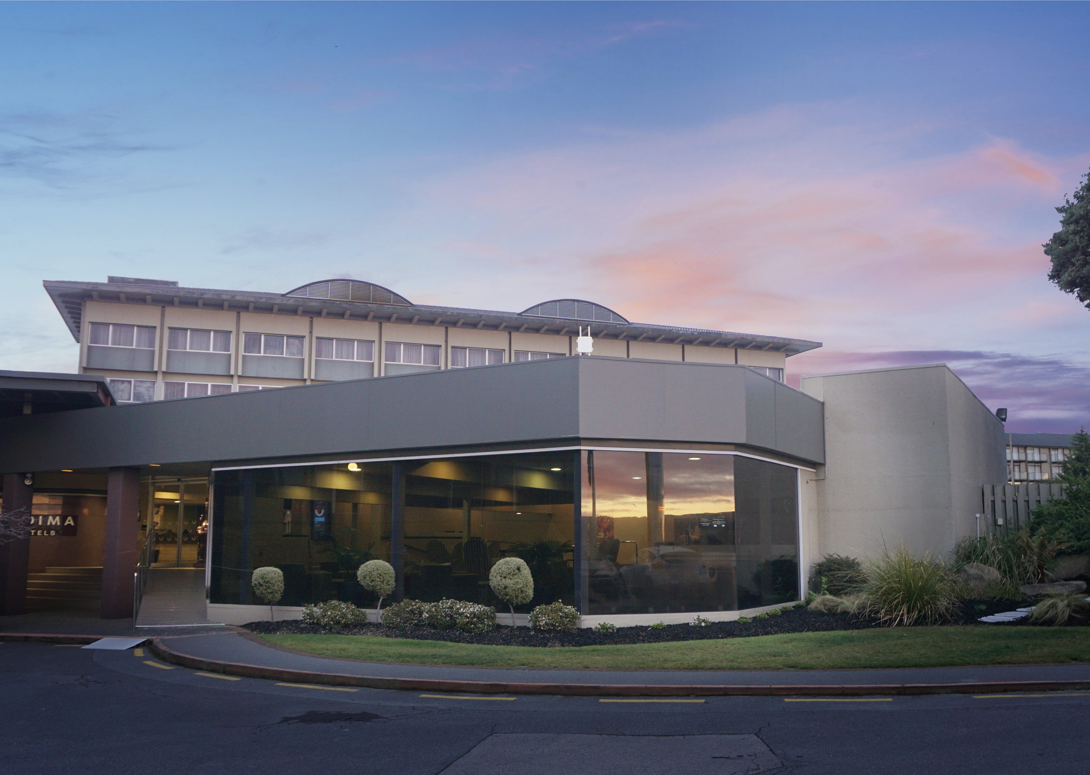 Exterior side view of the hotel’s lobby. Cream and gray building with stunning landscape outside and wide glass windows.