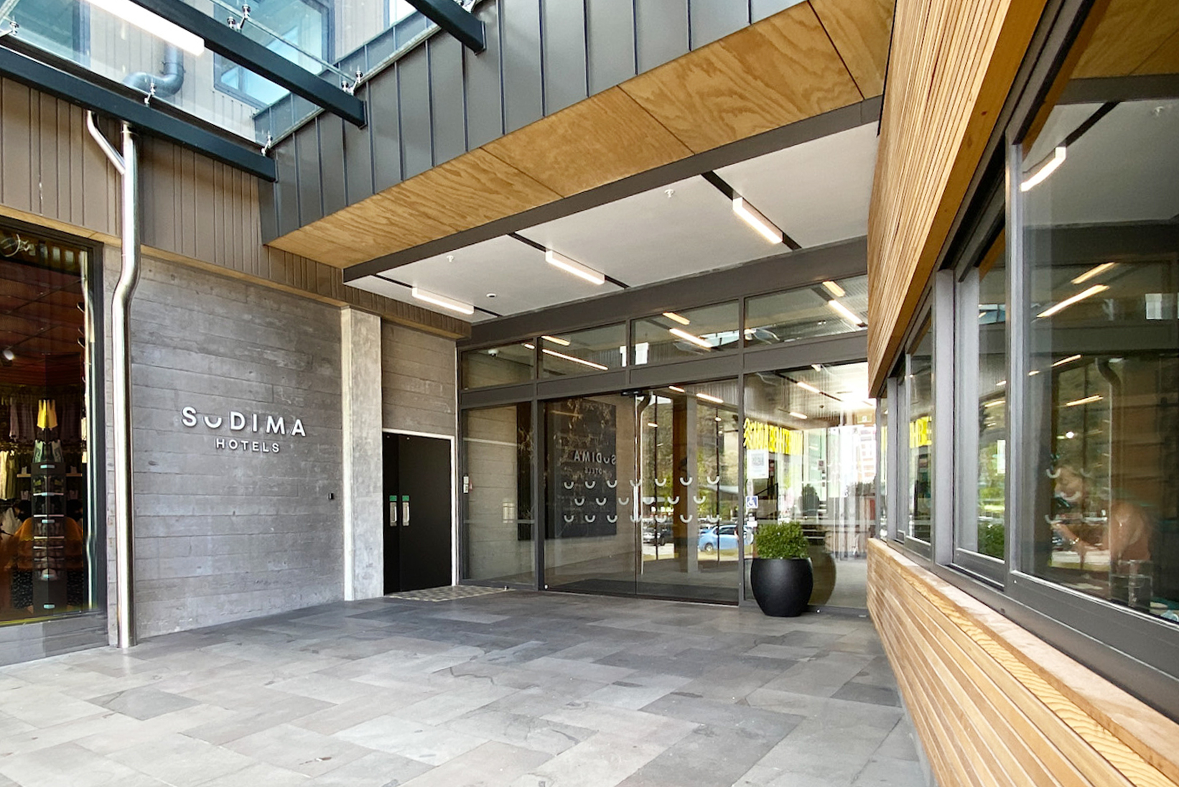 Front view of sudima hotels main entrance. it features a huge automatic glass door to go along with wood and granite finishes on both sides.